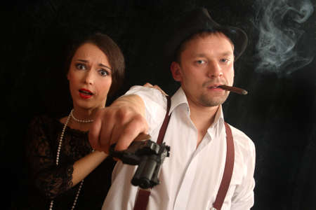 Portrait of the man in a hat with a cigar and a pistol and the beautiful woman. In style of a retro.の写真素材