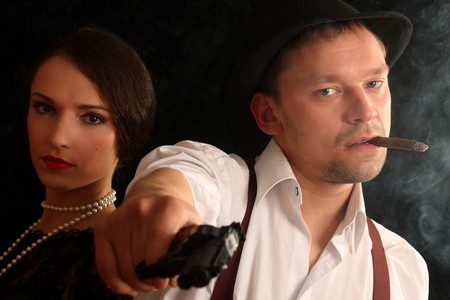 Portrait of the man in a hat with a cigar and a pistol and the beautiful woman. In style of a retro.の写真素材