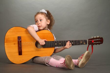 the little girl sits on a floor with a big guitar, a look not in a lens, a double 2の写真素材