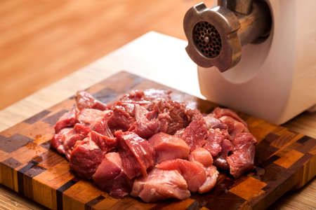 The electric meat grinder and the cut meat on a wooden chopping board