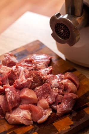 The electric meat grinder and the cut meat on a wooden chopping boardの写真素材