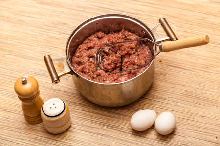 Mincemeat in a metal pan, eggs, a pepperbox and a saltcellar on a kitchen tableの写真素材