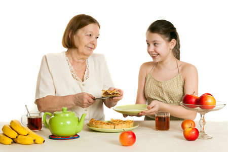 the grandmother treats the granddaughter with pie at a tableの写真素材