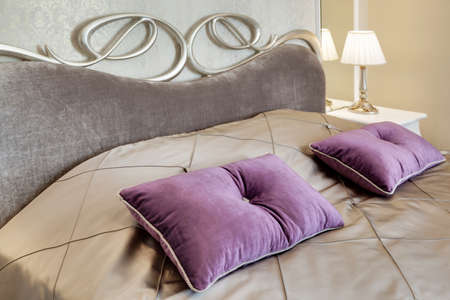 little table with a lamp and a bed with pillows in a modern bedroomの写真素材