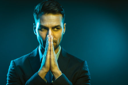 Serious Business Man Has an Idea How to Improve His Business. Strong White Man With Folded Hands in Creative Neon Light. Close-Up Portrait on Blue Background. High quality photoの写真素材