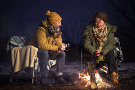 In love mature couple romantic dinner at campfire drinking hot natural tea sitting on the plaid...