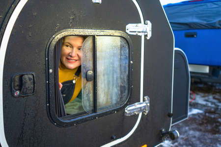 Red head middle aged woman looking out of the camper window. Family vacation time together at the journey enjoying time in camper trailer. Vacation and journey concept. Camper trailer journey concept.の写真素材