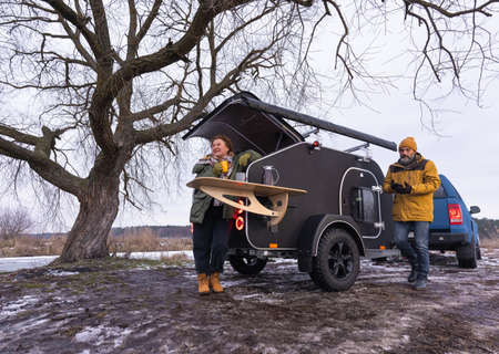 Middle aged couple kissing while drink hot morning coffee standing nest to a camper. Mature couple...