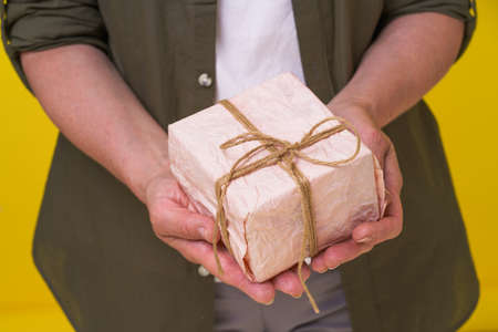 Mature woman with gift box in hands isolated on yellow background. Senior woman with a gif wrapped...