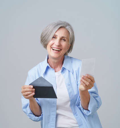 Mature woman with grey hair holding fancy envelop with gift card or certificate, with pleasant...