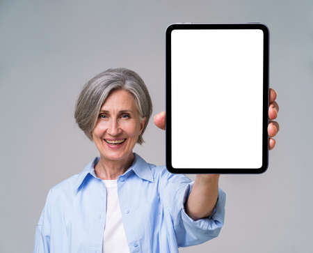 Happy confident mature woman holding digital tablet with white empty screen. Digital tablet in hands...