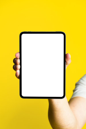 Digital tablet with white screen in man hand isolated on yellow background. mobile application advertisement. Product placement copy space.の写真素材