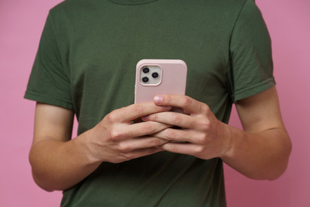 No face visible. Teenager boy with smartphone in hands isolated on pink background. Teenager guy in...