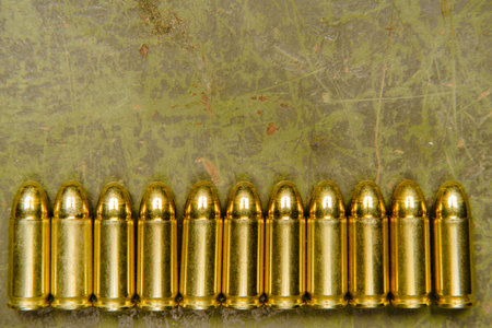 Golden pistol rounds or bullets, specifically 9x21, arranged on old, scratched green metal...
