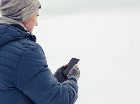 Handsome and happy guy with mobile phone in a snowy fieldの写真素材