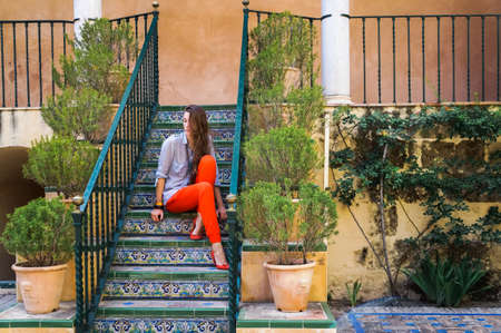 Cute young woman strolling along beautiful streets among old houses and green plants
