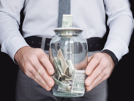 transparent glass jar that is used by a young man as a piggy bankの写真素材