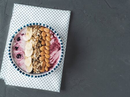 Healthy food - berry smoothie and muesli made from oatmeal, almonds, banana and blueberries, in a beautiful plate on a gray table, close-up, top viewの写真素材