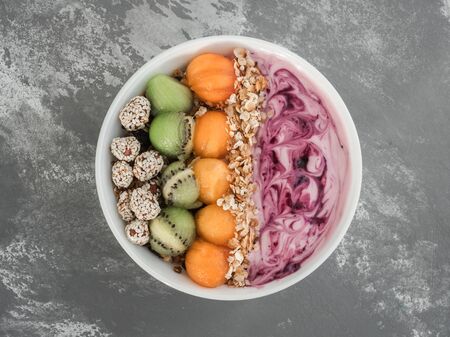 Healthy and delicious food - berry smoothie and muesli with nuts and sesame seeds, pieces of kiwi and persimmon in a white plate on a stylish gray table, close-up, top viewの写真素材