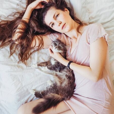 Beautiful, young woman lying in bed with her charming catの写真素材