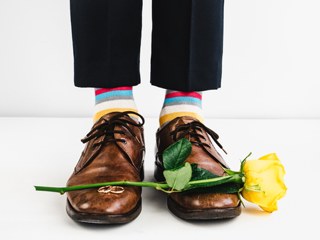 Wedding rings, yellow rose, bright, funny socks and man's legs in stylish brown shoes on a white background. Wedding preparationsの写真素材