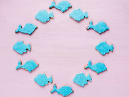 Fresh holiday cookies in the shape of fish in blue glaze on a pink background. Top view of a close-up. Holiday, romance, beautyの写真素材