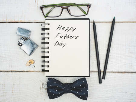 Silk bow tie, pen, pencil and notepad with handwritten congratulations on Father's day on a beautiful, white table. View from the top. Concept of a happy family, fashion and eleganceの写真素材