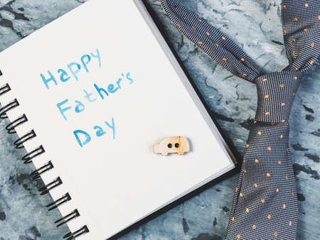Silk bow tie and notepad with handwritten greeting on Father's day on a beautiful, grey table. View from the top. Concept of a happy family, fashion and eleganceの写真素材
