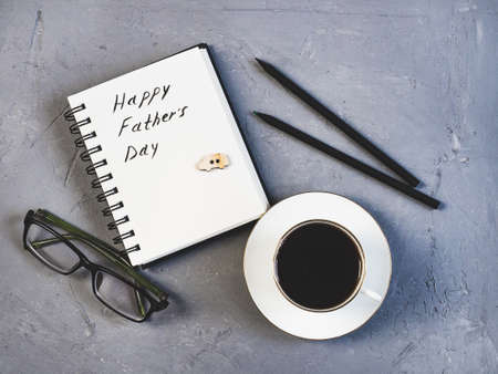 Cup of coffee, glasses, pen, pencil and notepad with handwritten congratulations on Father's day on a beautiful, gray table. View from the top. Concept of a happy familyの写真素材
