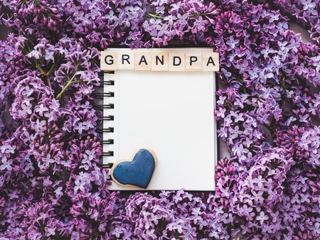 Heart-shaped cookie, covered with bright glaze, word GRANDPA, notepad with a blank page for Your inscription on the background flowers. Top view, close-up. Congratulations for relatives, loved onesの写真素材