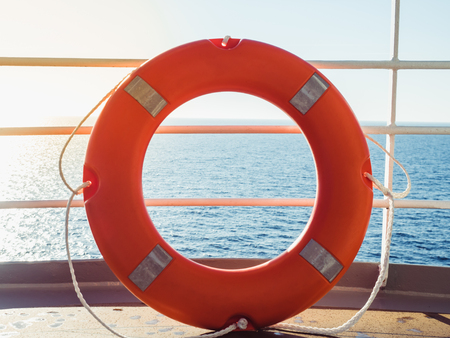 Bright, orange lifebuoy on the top deck of the cruise liner on the background of the sea waves and the morning sun. Concept of security, care and assistanceの写真素材