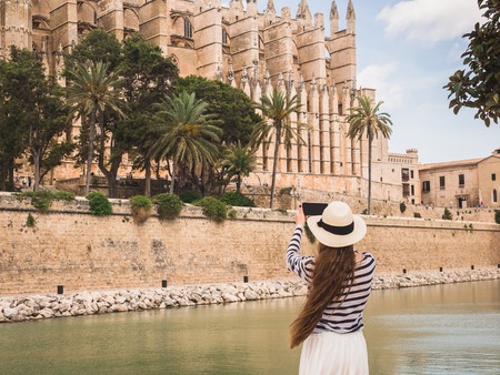 Stylish, happy woman with a smartphone on the background of a river, palm trees and historic, famous...