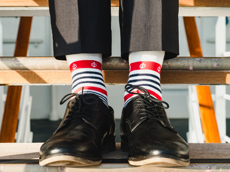 Man in stylish, black shoes, dark pants and funny, bright, striped socks with a pattern on the deck of a cruise ship. Lifestyle, fashion, funの写真素材