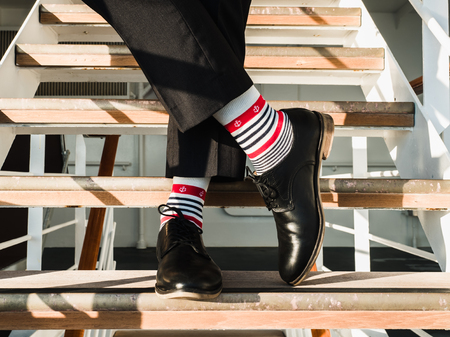 Man in stylish, black shoes, dark pants and funny, bright, striped socks with a pattern on the deck of a cruise ship. Lifestyle, fashion, funの写真素材