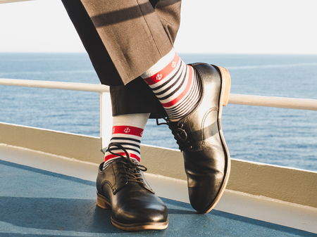 Man in stylish, black shoes, dark pants and funny, bright, striped socks with a pattern on the deck of a cruise ship. Lifestyle, fashion, funの写真素材