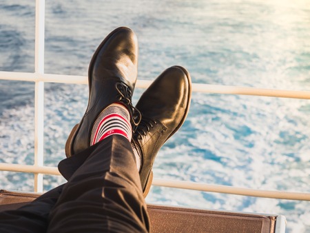 Man in stylish, black shoes, dark pants and funny, bright, striped socks with a pattern on the deck of a cruise ship. Lifestyle, fashion, funの写真素材