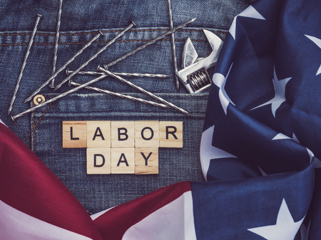 USA flag, tools, and wooden letters with the inscription LABOR DAY on the background of a blue jeans...