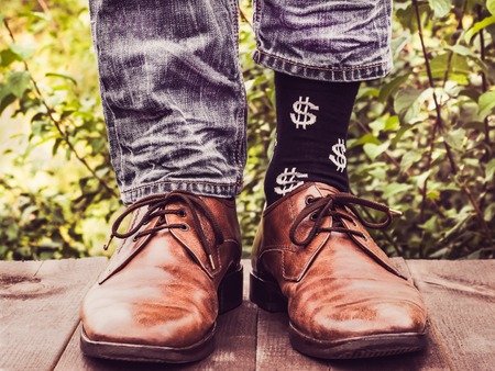 Men's legs in stylish shoes, black socks with patterns in the form of US dollars on a wooden terrace against the background of green trees. Beauty, fashion, eleganceの写真素材
