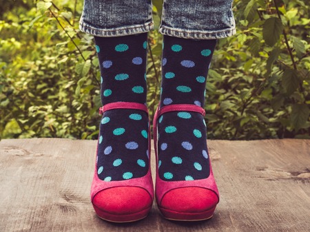 Women's legs in stylish shoes, bright, variegated, multi-colored socks on the wooden terrace on the background of green trees. Lifestyle, fashion, beauty, funの写真素材