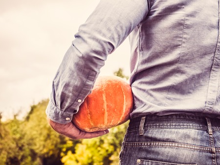 Young man in a denim shirt holding a ripe pumpkinの写真素材