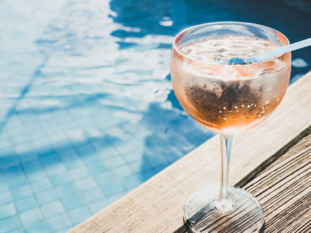 Beautiful glass with a pink cocktail and ice cubes on the background of the pool with blue water. Top view, close-up. Rest during a sea cruiseの写真素材