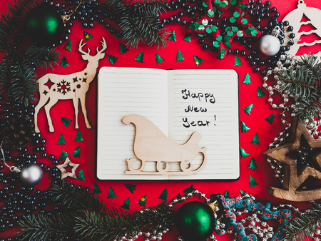 Colorful New Year and Christmas decorations, silver beads, branches of the Christmas tree, drawing in a notebook on a red surface. Top view, close-up, flat lay. Greeting cardの写真素材