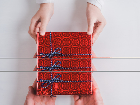 Bright box with a gift, tied with a ribbon, hands of a loving father and hands of a child on a white, isolated background. Top view, close-up. Preparing for the holidays. Happy family conceptの写真素材