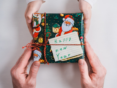 Bright box with a gift, tied with a ribbon, hands of a loving father and hands of a child on a white, isolated background. Top view, close-up. Preparing for the holidays. Happy family conceptの写真素材