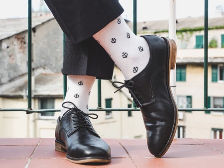 Men's legs, stylish shoes, colorful socks with a pattern in the form of anchors on the background of the street and houses. Concept of style, fashion and beautyの写真素材