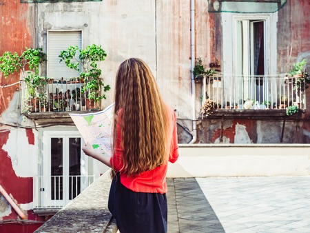 Cute woman holding a map, against the background of old houses in the beautiful city of Naples,...