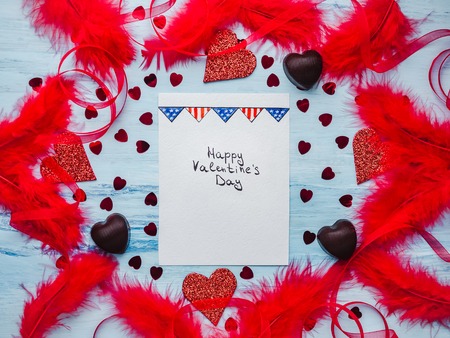 Note with sweet words of love, ribbons, colorful feathers, candy and tinsel in the shape of a heart. Top view, isolated background. Congratulations for loved ones, relatives, friends and colleaguesの写真素材