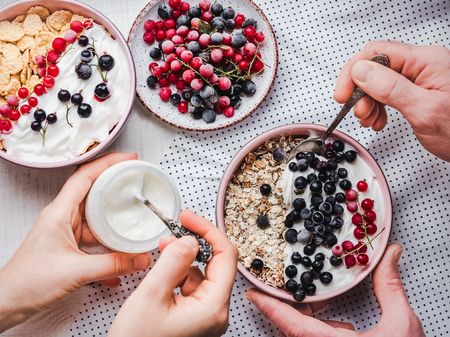Festive and healthy breakfast for loved ones. Vintage bowls, cornflakes, granola, yogurt, fresh berries and hands of a young couple. Close-up, top view. Concept of healthy and delicious foodの写真素材