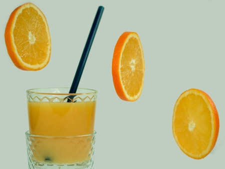 Glass with fresh orange juice, flying orange slices on a white, isolated background. Close-up. Concept of tasty and healthy foodの写真素材