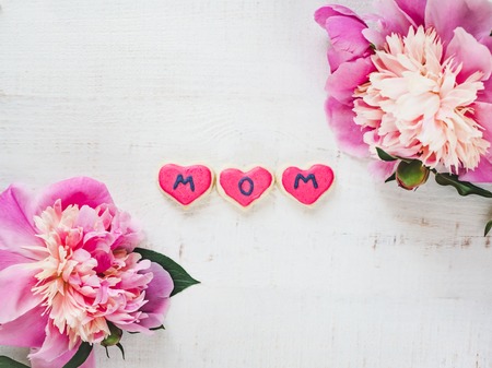Bright flowers and pink, glazed cookie with the word MOM on a white, isolated background. Top view, close-up. Happy family conceptの写真素材